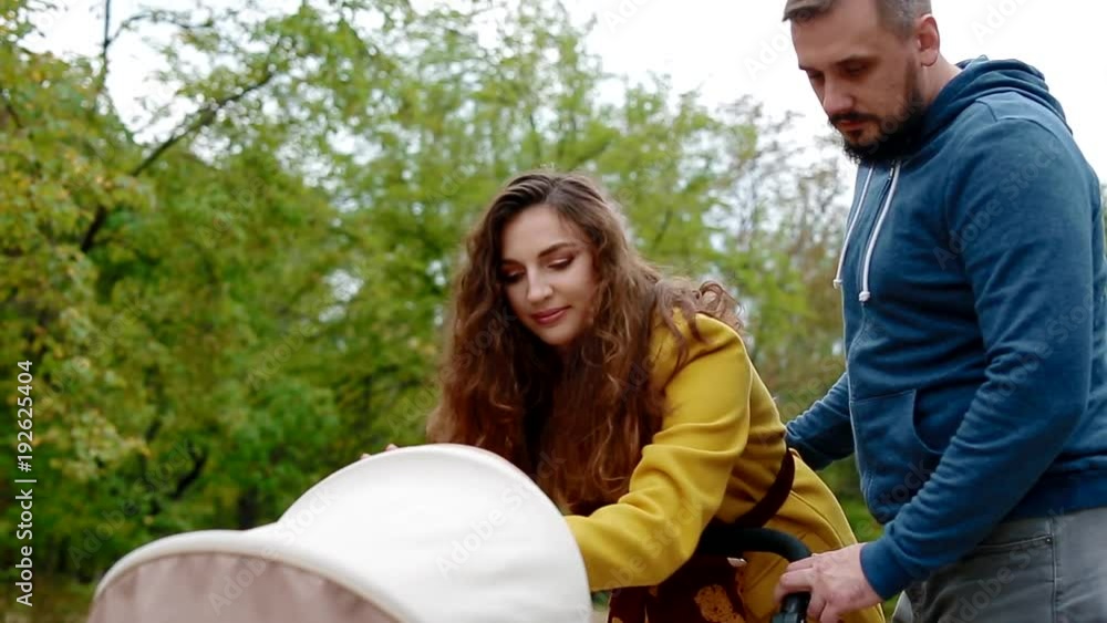 Young family walking with newborn child. White woman looking in to baby carriage Young family walking with newborn child. White woman looking in to baby carriage