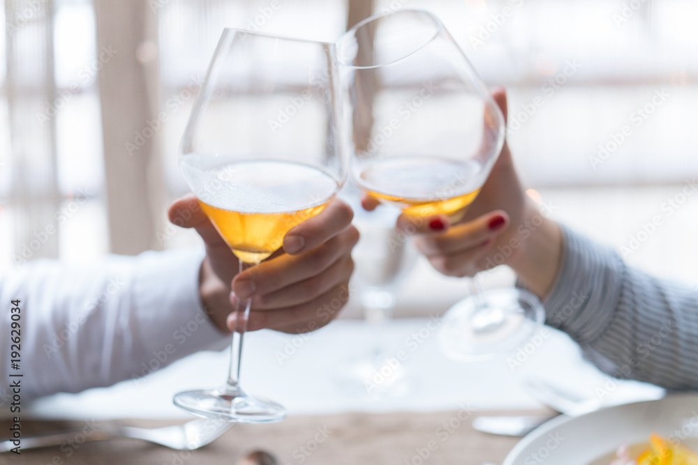 Close up portrait of a female and male hands toasting with glasses of white wine over table