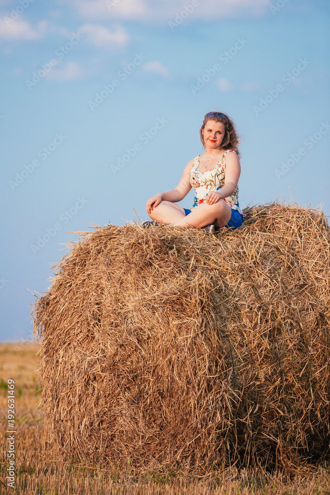 Beautiful Plus Size Young Woman In Shirt Sit Near Hay Bales In Summer Beautiful Plus Size Young Woman In Shirt Sit Near Hay Bales In Summer