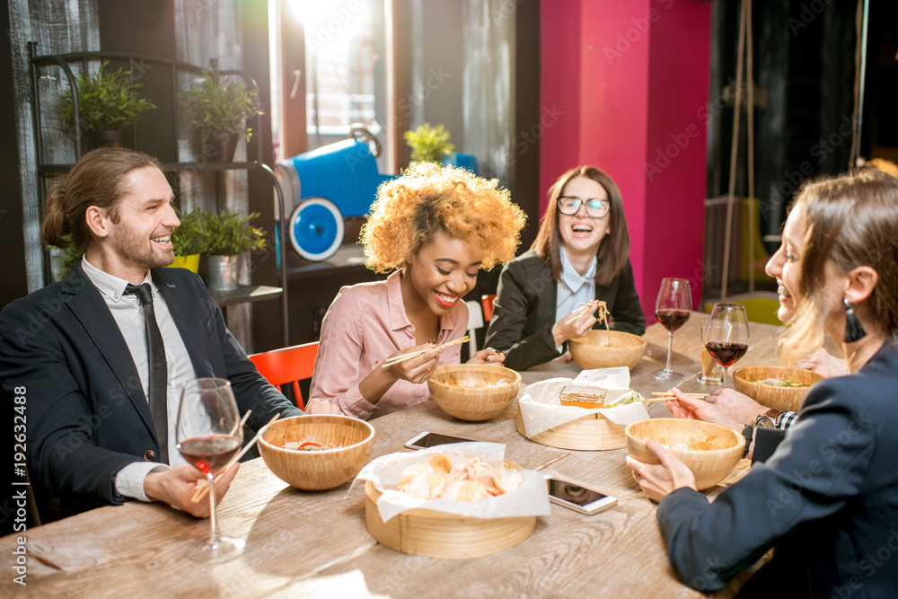 Multi ethnic group of business people sitting at the table during the dinner with asian food in the modern restaurant