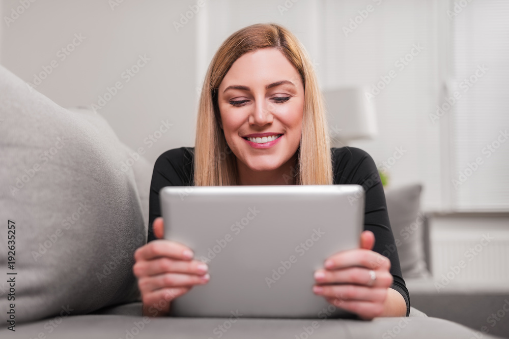 Attractive woman using a tablet pc while lying on the couch at home. Attractive woman using a tablet pc while lying on the couch at home.