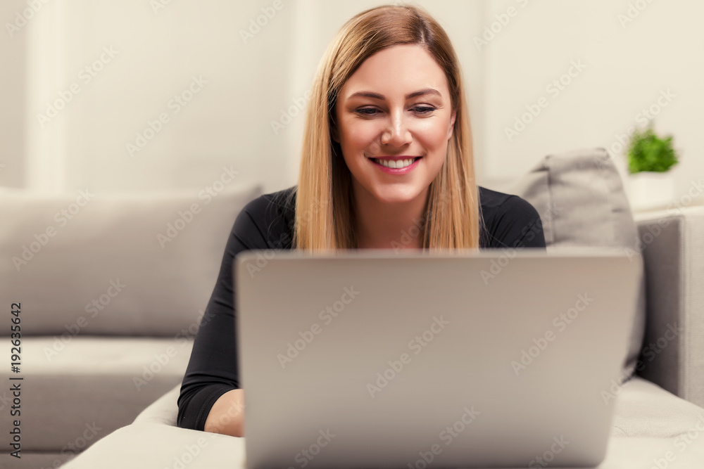 Attractive woman using a laptop while lying on the couch at home. Attractive woman using a laptop while lying on the couch at home.