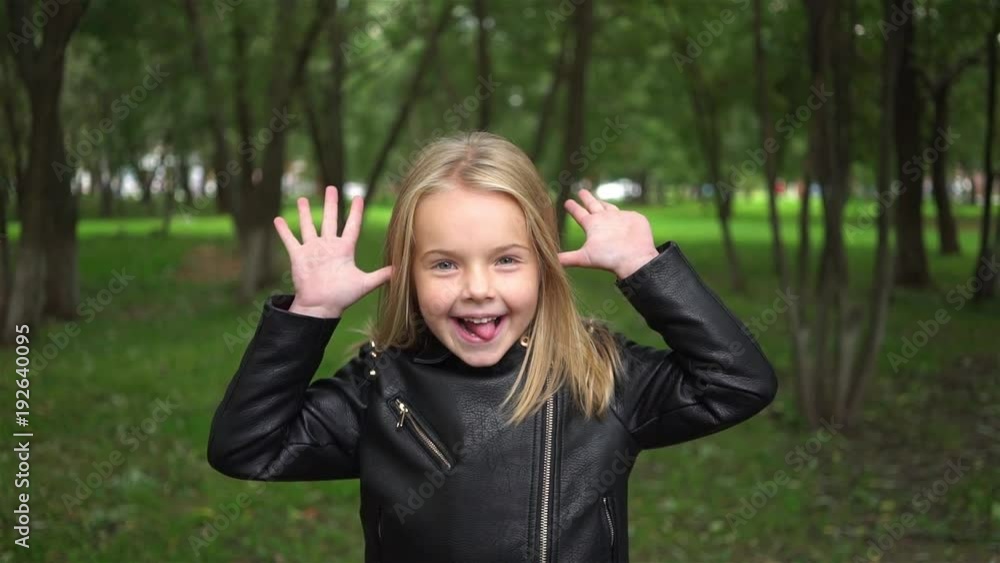 Cute little blonde girl making funny faces in a park on a cloudy summer day. Handheld slow motion medium shot Cute little blonde girl making funny faces in a park on a cloudy summer day. Handheld slow motion medium shot