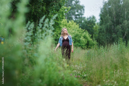 young beautiful pregnant woman is walking in the park or blossoming field