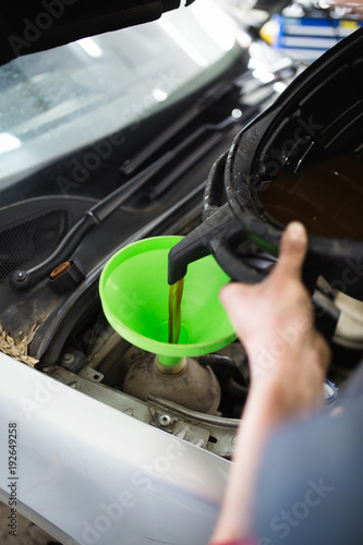 Car repair service center work. Mechanic man worker pouring antifreeze from small bottle in the cooling system. © Dusko