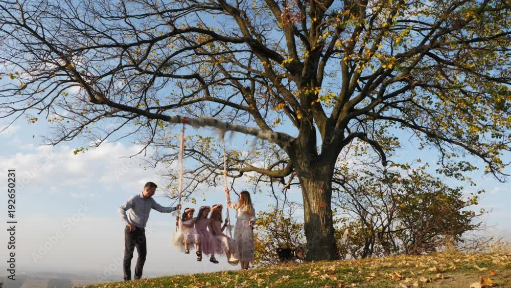 Father and mother shakes her daughters on a swing under a tree. Father and mother shakes her daughters on a swing under a tree.