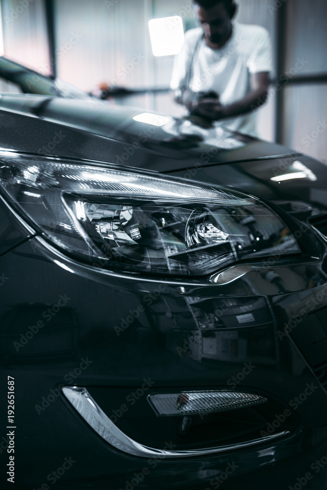 Fototapeta premium Car detailing - Hands with orbital polisher in auto repair shop. Selective focus.