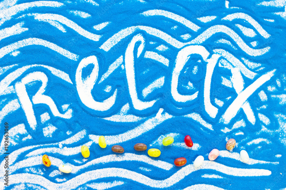 Relax inscription on a blue colored sand with waves, candies, top view, flat lay Relax inscription on a blue colored sand with waves, candies, top view, flat lay