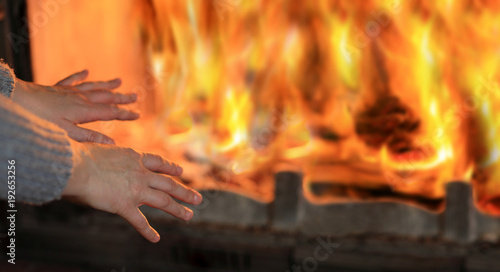 Ogień w kominku, kobieta grzeje dłonie.
