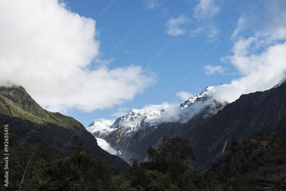 Paisaje de picos de montañas nevados y verdes con cielo nublado en Nueva Zelanda