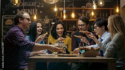 In the Bar/ Restaurant Group of Diverse Young People Eat Slices of Pizza Pie. They Talk, Tell Jokes and Have Fun in This Stylish Establishment.