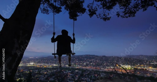 Man swinging on swings at night on top of mountain overlooking city Los Angeles