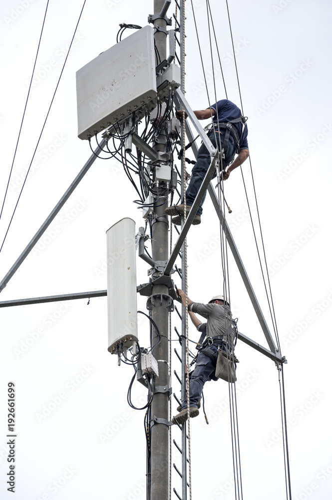 Naklejka premium Workers climb up for a maintenance operation to a telephone repeater