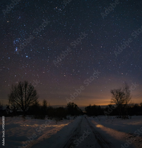 The road in Russian village , frosty and snowy at night. The trees and the starry sky overhead. The constellation of Orion shines in the sky. © dmitriydanilov62