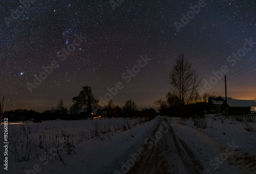 The road in Russian village , frosty and snowy at night. The trees and the starry sky overhead. The constellation of Orion shines in the sky.