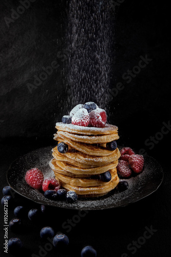 a stack of pancakes decorated with berries and powdered sugar, rustic studio shot, can be used as background photo