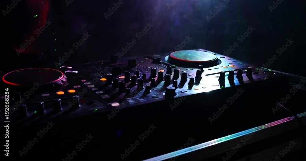 DJ Spinning, Mixing, and Scratching in a Night Club, Hands of dj tweak various track controls on dj's deck, strobe lights and fog, selective focus, close up. Slider Shoot