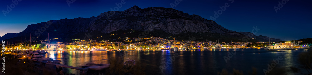 A beautiful view of the seaport full of ships and boats, and a city illuminated at night, at the foot of the mountains