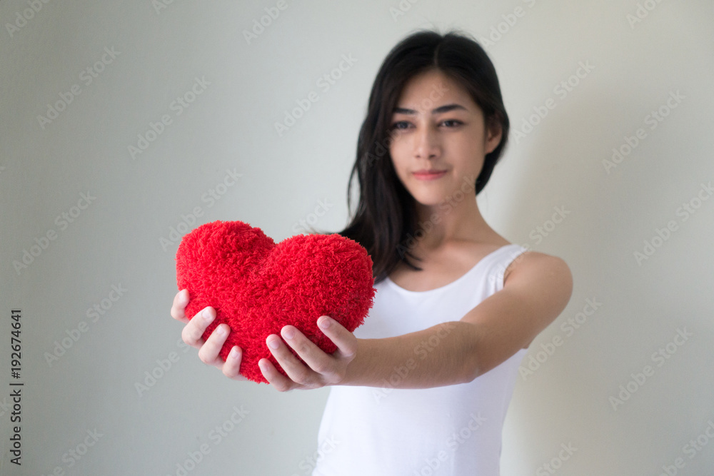 Focus hand holding red heart.Happy beautiful young woman holding red cushion heart shape smiling and looking at camera.love romance and valentines day concept. Focus hand holding red heart.Happy beautiful young woman holding red cushion heart shape smiling and looking at camera.love romance and valentines day concept.