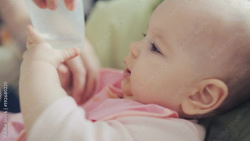 little girl drinking from a plastic Cup. the girl is smeared with baby food and dressed in pink bib little girl drinking from a plastic Cup. the girl is smeared with baby food and dressed in pink bib