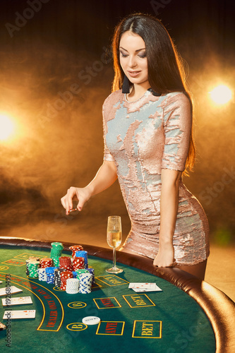 Gorgeous young woman in evening dress standing near poker table with glass of champagne photo