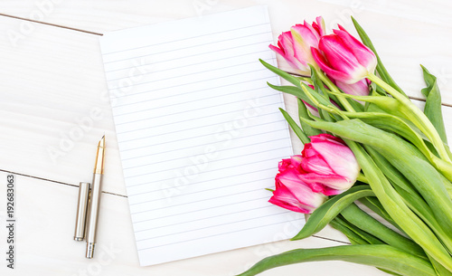 Blank notepad and bouquet with tulips on the wooden table. Top view.
