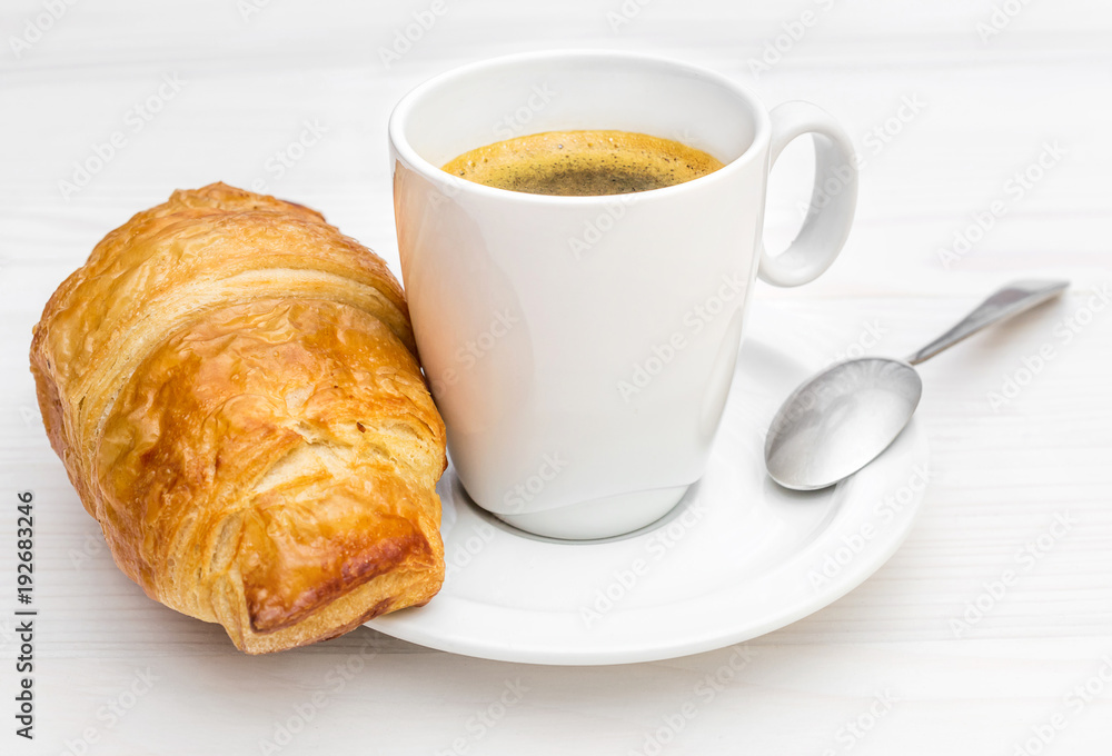 Cup of coffee and croissant on the saucer. Close up. Cup of coffee and croissant on the saucer. Close up.