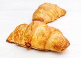 Two fresh croissants on white wooden table. Close up.