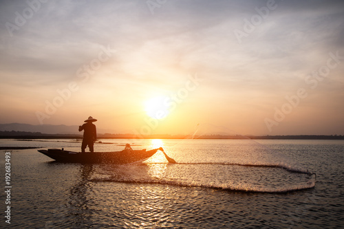 Asian fisherman throwing fishing net in lake at sunrise time.(Lifestyle of the population living in the river)