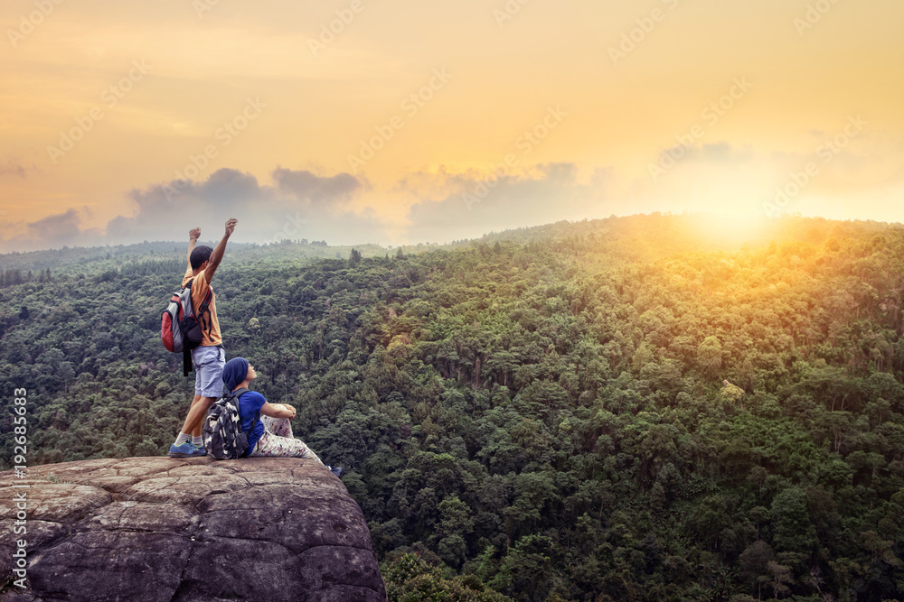 couples of traveling man and woman relax on top of  high mountain with beautiful sunset sky behind green mountain