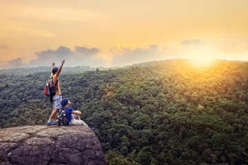 couples of traveling man and woman relax on top of  high mountain with beautiful sunset sky behind green mountain