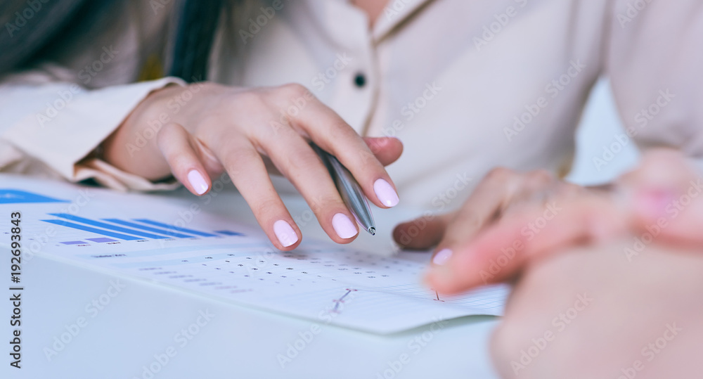 Business woman hand holding pen and pointing at financial diagram, graph during conference sitting at the office desk.