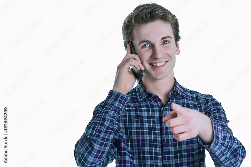 Casual smiling man talking on his mobile phone and pointing with finger to the camera on white background. Casual smiling man talking on his mobile phone and pointing with finger to the camera on white background.