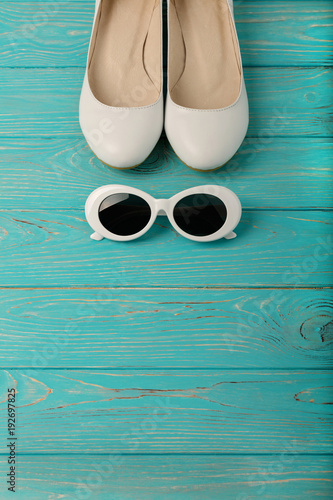 Women's shoes and white sun glasses on a blue wooden background.