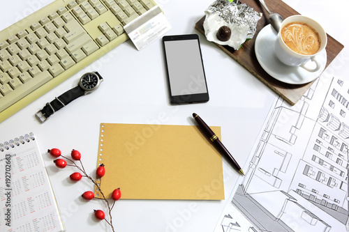 Widok biurka architekta z góry z klawiaturą, kawą i szkicem budynku.