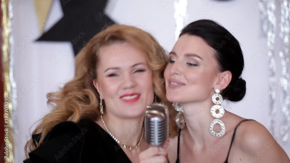 Two charismatic girls in evening dresses sing at a party Two charismatic girls in evening dresses sing at a party
