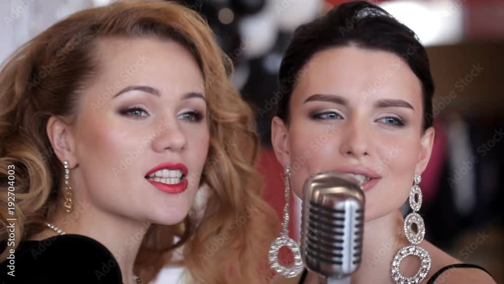 Two charismatic girls in evening dresses sing at a party