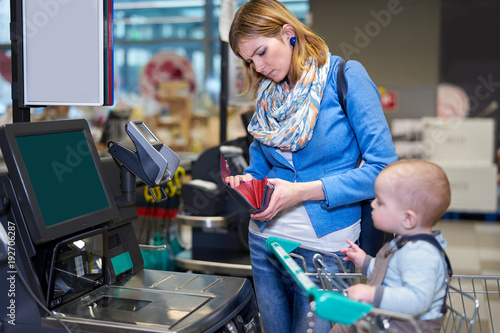 Billede på lærred Young woman with baby paying with self checkout