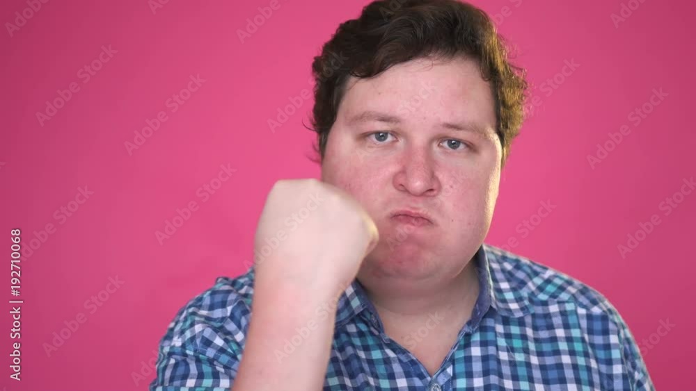 Enraged nervous man threatens someone with his fist and is making an admonition isolated on pink background Enraged nervous man threatens someone with his fist and is making an admonition isolated on pink background