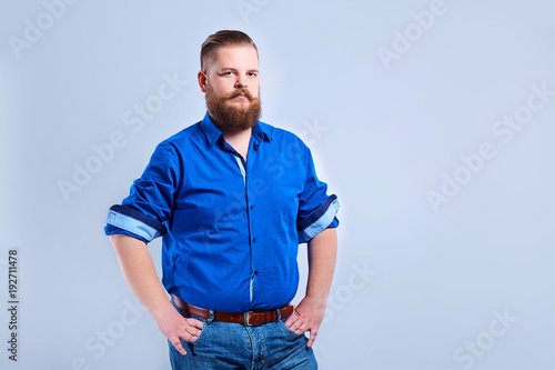 A fat, bearded man looks at the gray background with a serious expression of emotion.