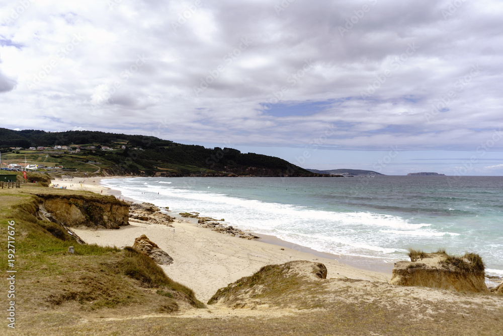 View of the Razo beach on the Atlantic ocean and green mountains to the background on a summer day with many clouds in a landscape typical of Galicia, Spain.