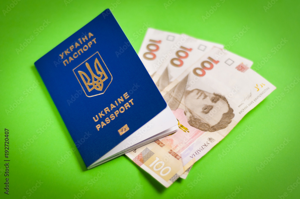 One blue biometric ukrainian foreign passport with gold color inscription and coat of arms on green background and three banknotes of one hundred hryvnias. Travel concept One blue biometric ukrainian foreign passport with gold color inscription and coat of arms on green background and three banknotes of one hundred hryvnias. Travel concept