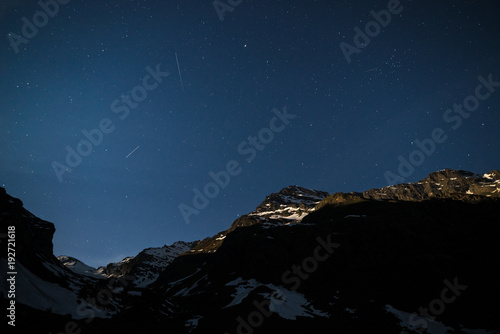 The starry sky on the Alps illuminated by moonlight. Expansive night landscape wide view.