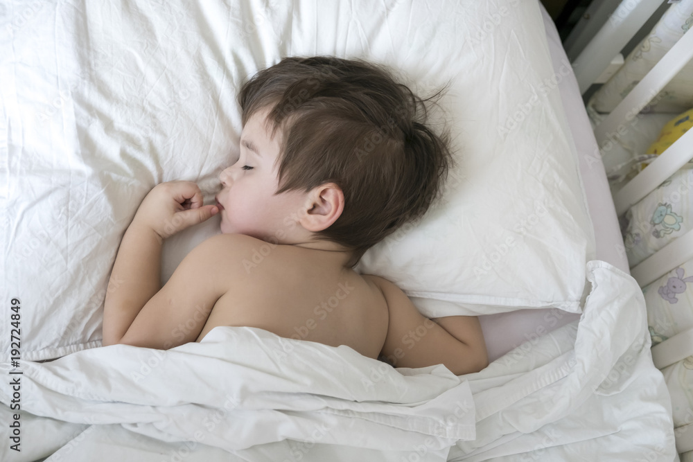 Peaceful baby lying on a bed while sleeping in a bright room. cute two year old Asian boy on white the pillow Peaceful baby lying on a bed while sleeping in a bright room. cute two year old Asian boy on white the pillow