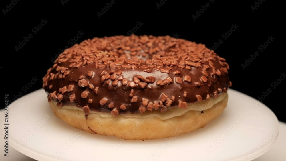Sweet chocolate donut with brown sugar crystals rotating on dark background Sweet chocolate donut with brown sugar crystals rotating on dark background