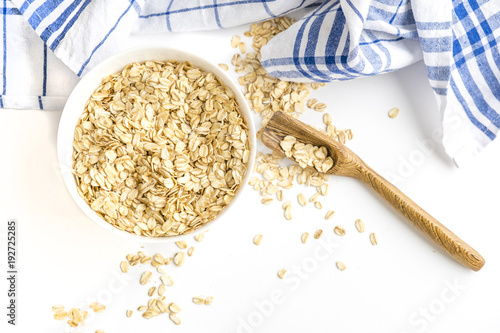 Rolled oats flakes breakfast. Dry oatmeal in bowl isolated on white background. Top view. Delicious Vegan food a hearty cereal photo