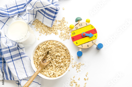 Rolled oats flakes breakfast. Dry oatmeal in bowl isolated on white background. Top view. Delicious Vegan food a hearty cereal. multicolored clock, diet time photo