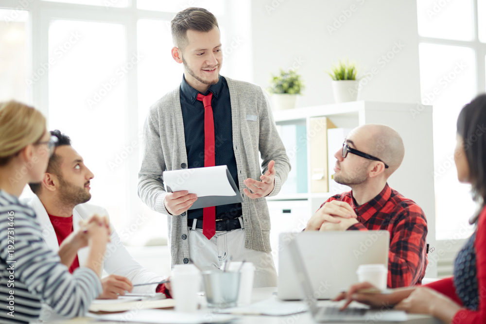 Young businessman in smart casual looking at one of employees while explaining his ideas or points of report