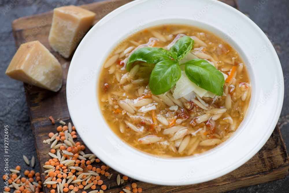 Close-up of italian soup with red lentil, pasta and addition of parmesan served in a white plate, studio shot, selective focus Close-up of italian soup with red lentil, pasta and addition of parmesan served in a white plate, studio shot, selective focus