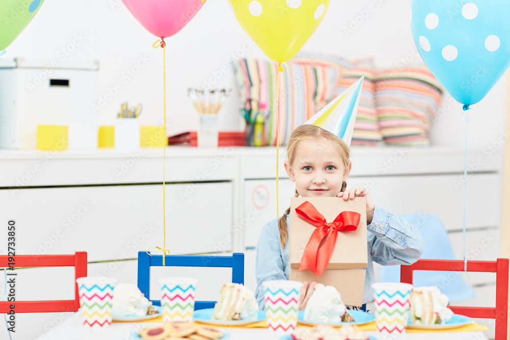 Cute girl opening giftbox while sitting by served table on her birthday party Cute girl opening giftbox while sitting by served table on her birthday party